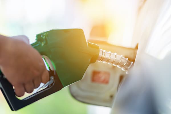 Man Handle pumping gasoline fuel nozzle to refuel. Vehicle fueling facility at petrol station. White car at gas station being filled with fuel. Transportation and ownership concept.
